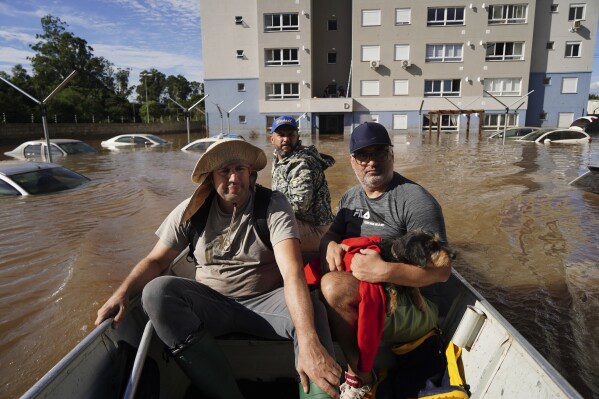 Pessoas resgatam uma cadela chamada Maya de uma área alagada após fortes chuvas em Canoas, Rio Grande do Sul, Brasil, quinta-feira, 9 de maio de 2024. (AP Photo/Carlos Macedo)