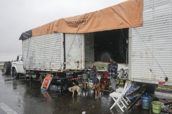 Pessoas que perderam suas casas devido às enchentes vivem em uma carreta de caminhão em Canoas, Rio Grande do Sul, Brasil, sexta-feira, 10 de maio de 2024. (AP Photo/Andre Penner)