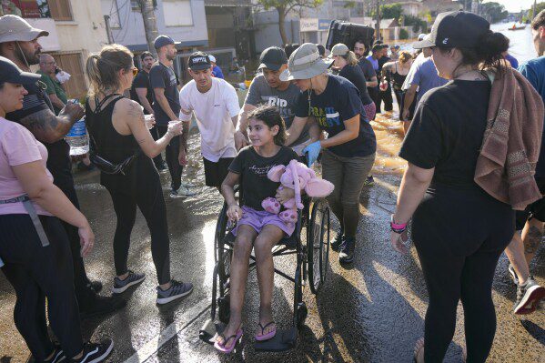 Voluntários empurram uma cadeira de rodas transportando um evacuado de uma área inundada por fortes chuvas, em Porto Alegre, Brasil, terça-feira, 7 de maio de 2024. (AP Photo/Andre Penner)