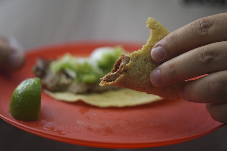 Um cliente segura um taco parcialmente comido na barraca de tacos Tacos El Califa de León, na Cidade do México, quarta-feira, 15 de maio de 2024. Tacos El Califa de León é a primeira barraca de tacos a receber uma estrela Michelin do guia gastronômico francês.  (Foto AP/Fernando Llano)