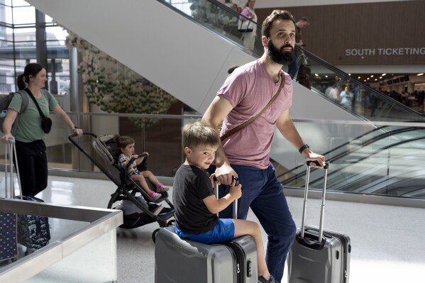 George Ridley, 4, à esquerda, anda em uma mala enquanto ele e seu pai, Chris Ridley, passam pelo Aeroporto Internacional de Nashville, quinta-feira, 23 de maio de 2024, em Nashville, Tennessee.  Espera-se que um número recorde de americanos viaje no fim de semana do Memorial Day de 2024. (AP Photo/George Walker IV)