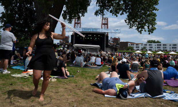 Uma mulher segura um bambolê e dança atrás de uma grande multidão de participantes do festival.