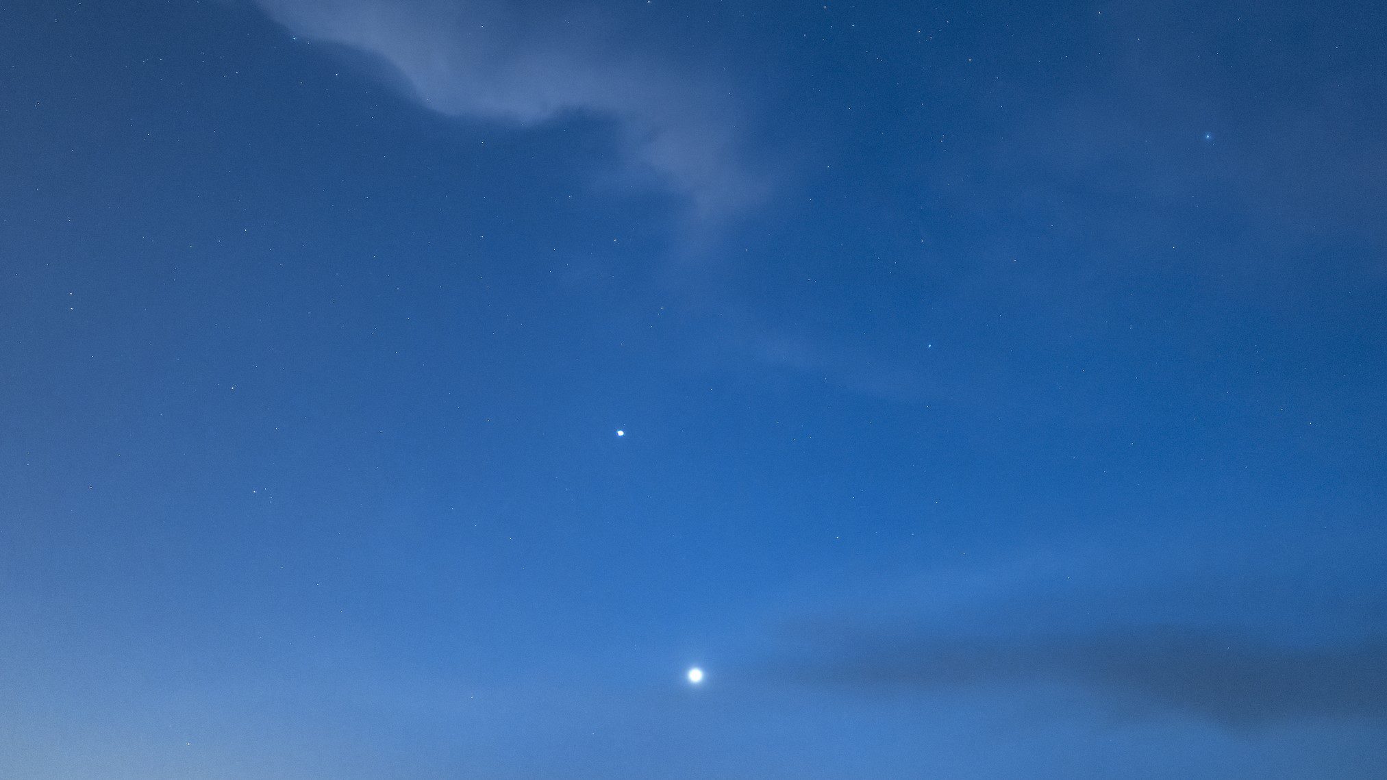 Céu azul escuro com nuvens fofas e dois pontos de luz brilhantes, um Vênus e outro Mercúrio.