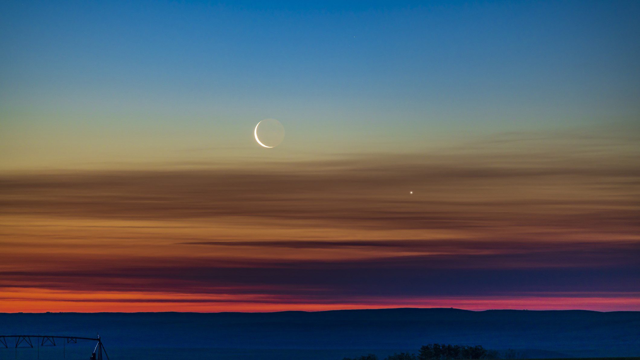 A conjunção do crescente minguante e Vênus conforme eles nascem no céu do amanhecer do nordeste, no sul de Alberta, Canadá. A luz da Terra pode ser vista no lado escuro da Lua. O céu mostra uma maravilhosa transição de cores do laranja no horizonte em todo o espectro para o azul no topo