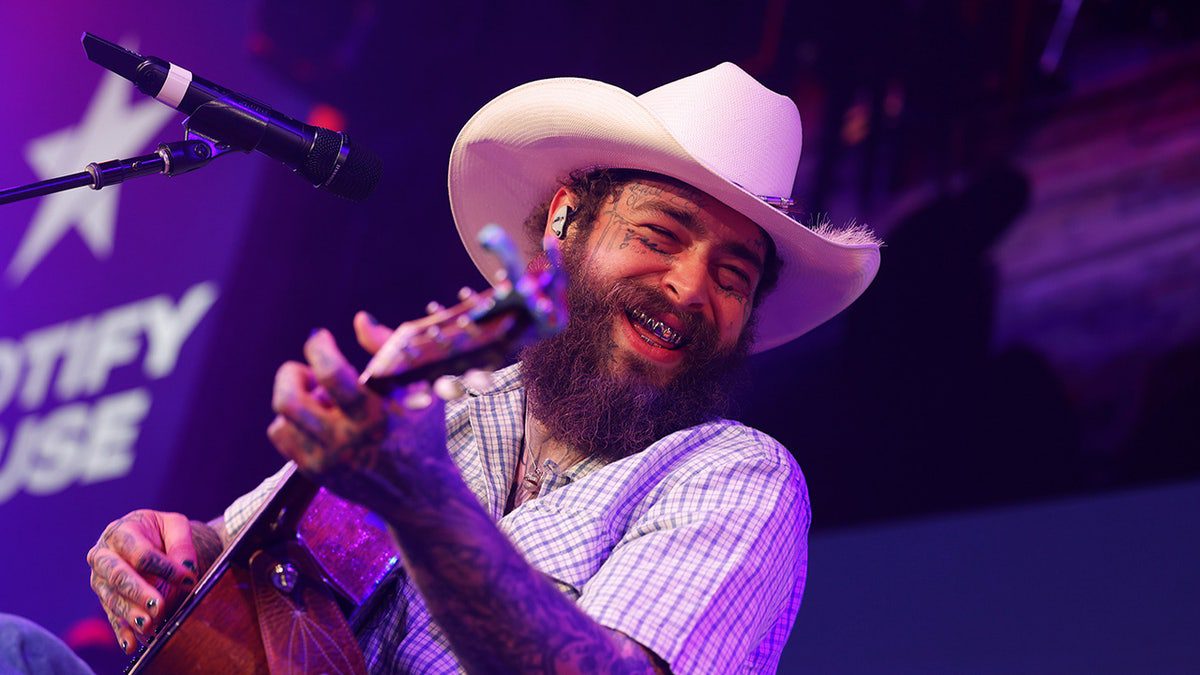 O músico Post Malone usa um chapéu de cowboy enquanto toca violão.