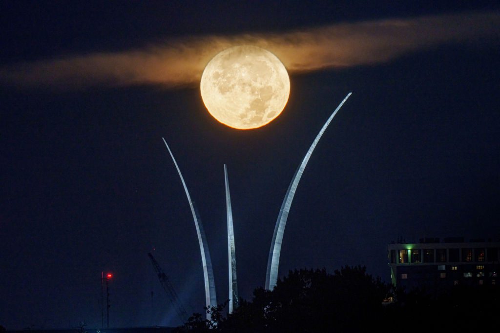 Uma estrutura alta de templo com uma lua grande e totalmente iluminada no topo.